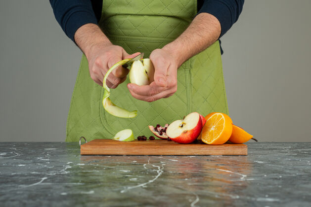 水果男手在桌上的木板上剥青苹果围裙有机橙子