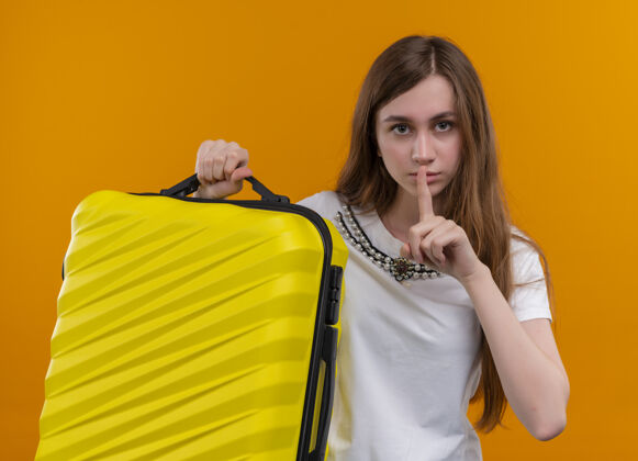 严肃神情严肃的年轻旅行家女孩拿着手提箱 在孤立的橙色空间里默默地做着手势旅行者橙色抱着