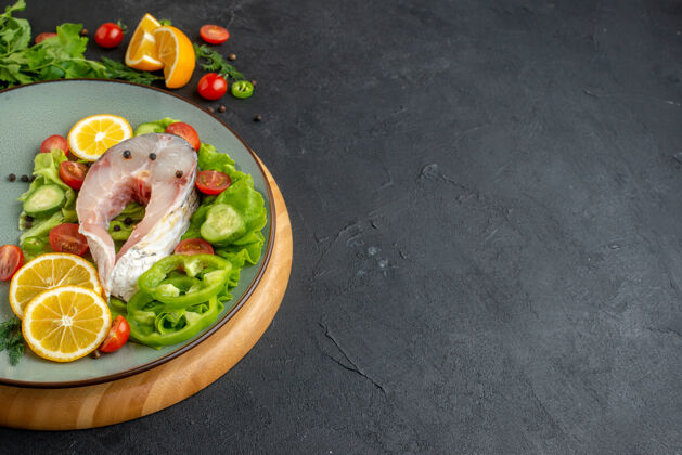 晚餐侧视图生鱼肉和新鲜切碎的蔬菜柠檬片香料在一个灰色的盘子上的一个圆板上的黑色苦恼的表面食物生鱼餐厅