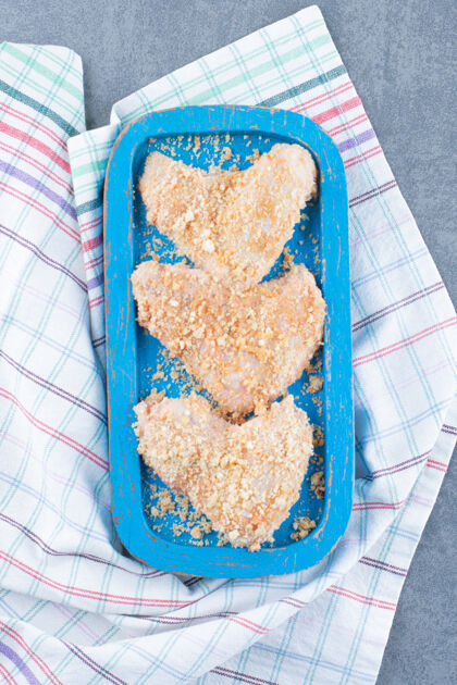 家禽生鸡翅配面包屑放在蓝色盘子里食物屠夫桌布