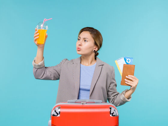 果汁正面图：度假中的女性拿着新鲜果汁和蓝色桌子上的机票海上度假飞机旅行前面旅程桌子
