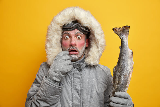 穿户外冬季活动和爱好概念目瞪口呆的男子红着冻僵的脸盯着的眼睛抱着钓到的大鱼穿着暖和的衣服已经成功捕鱼了季节角度兜帽