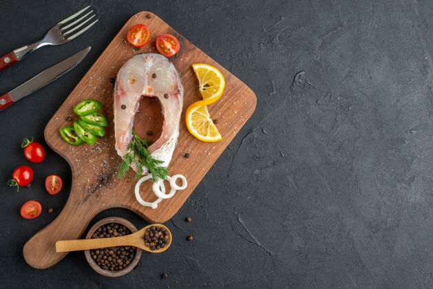 食物生鱼片和新鲜切碎蔬菜的俯视图柠檬片香料放在一个木板餐具上 餐具放在黑色的凹面右侧排骨盘子权利