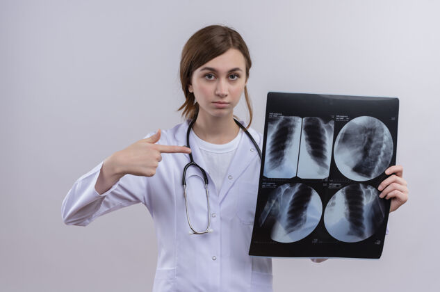 年轻面容严肃的年轻女医生穿着医用长袍 手持听诊器 拿着x光片指着它听诊器射击医生