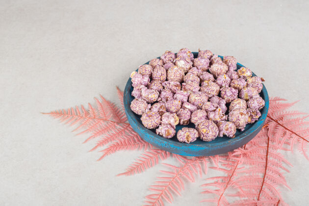 小吃破旧的木制托盘上放着美味的爆米花 放在大理石桌上一束粉红色的叶子上爆米花叶美味