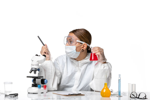 大流行正面图：女医生穿着防护服 戴着口罩 拿着一个装有红色溶液的瓶子 背景是淡白色的冠状病毒大流行病毒白色医疗外套