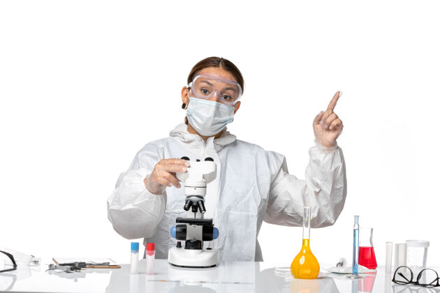 显微镜前视图女医生穿着特制的工作服 戴着口罩 用显微镜观察一种浅白色背景的冠状病毒大流行面具医生工作