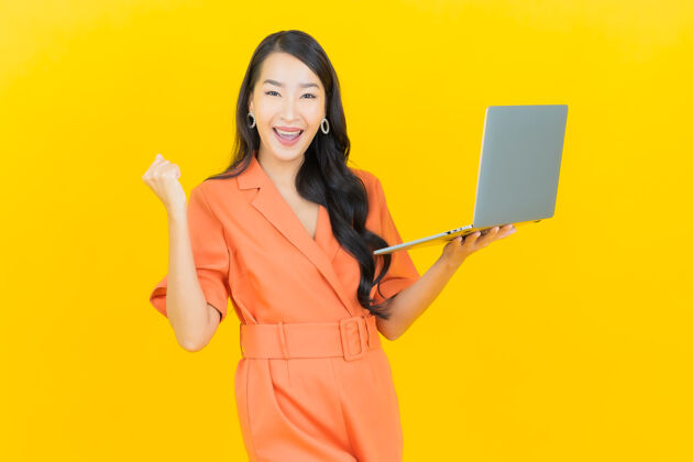 时尚肖像美丽的亚洲年轻女子微笑着用黄色笔记本电脑学生有趣办公室