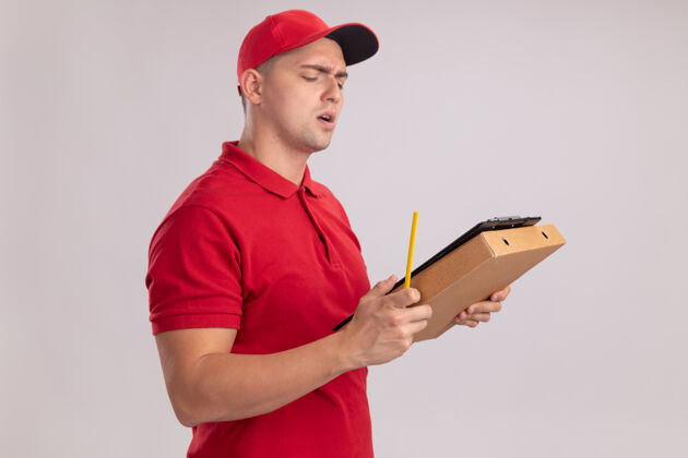人困惑的年轻送货员穿着制服戴着帽子拿着剪贴板和披萨盒-隔离在白墙上表情剪贴板站着