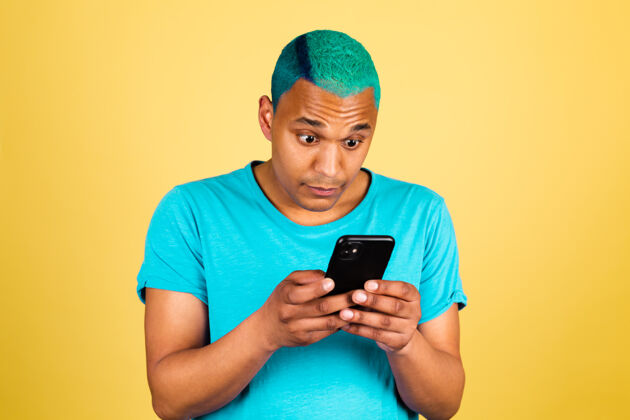 电话非洲黑人男子在黄色的休闲墙上用手机看着屏幕震惊地扬起眉毛手机美国人成人