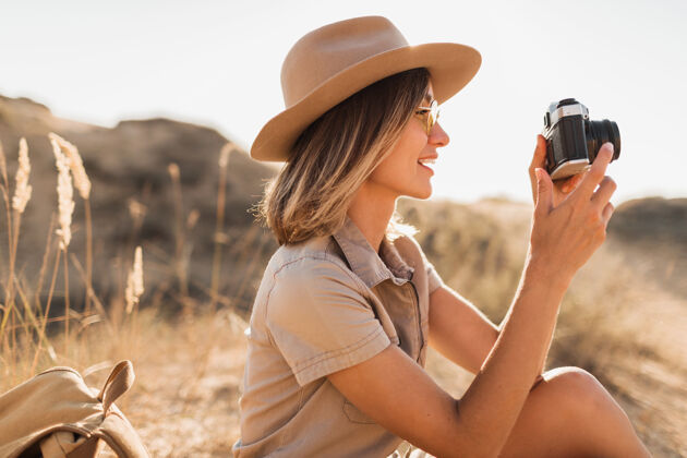 时尚沙漠中穿着卡其色长裙 在非洲旅行 戴着帽子 用老式相机拍照的迷人时尚年轻女子的肖像旅行休闲年轻人