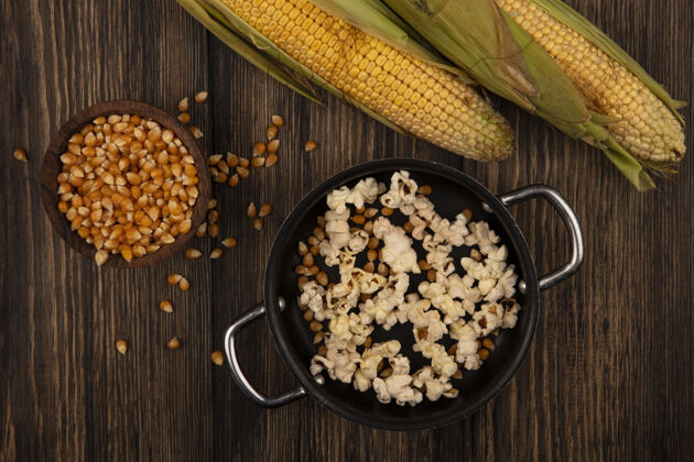 电影平底锅俯视图 美味的爆米花和新鲜的玉米粒放在木桌上的木碗里新鲜锅顶部