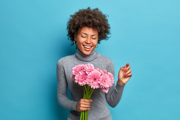 肖像一位留着卷发的快乐的年轻美国黑人妇女的肖像 手里捧着一束粉红色非洲菊 笑容灿烂高兴美甲花