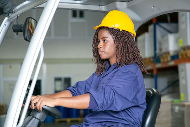 工厂穿着防护服的严肃年轻女物流工人在仓库里驾驶叉车车轮货物装运