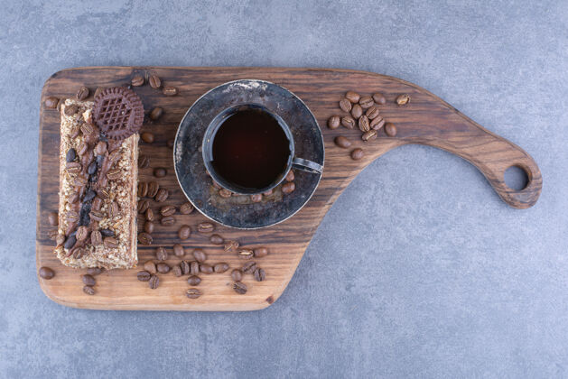 早餐一块蛋糕和咖啡豆旁边的一杯咖啡放在大理石表面的木板上饼干咖啡