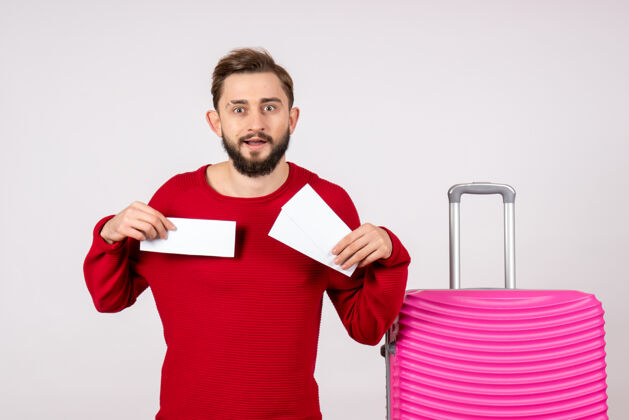 航班正面图：年轻的男性 带着粉色的包 拿着白墙航班的机票 彩色旅行 旅游度假成人年轻男性风景