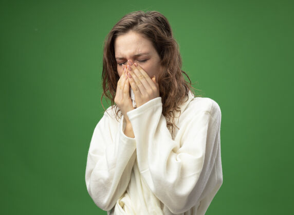 鼻子弱小的小女孩 闭着眼睛 穿着白袍 用餐巾擦鼻子 隔离在绿色的地板上餐巾疾病穿