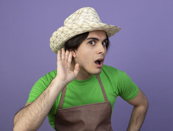 帽子可疑的年轻男园丁穿着制服 戴着园艺帽 表现出倾听的姿态男人男人穿着