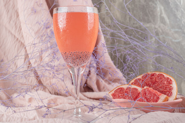 新鲜一杯果汁和新鲜的葡萄柚放在粉红色的布上柑橘果汁切片