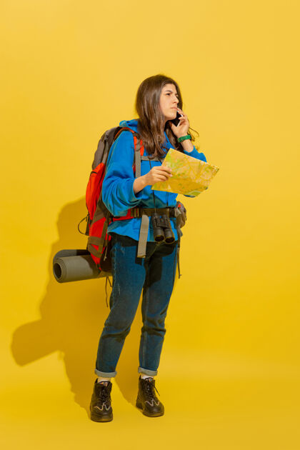 旅行用地图找路一个快乐的年轻白人旅游女孩的肖像 带着包和望远镜 隔离在黄色的工作室背景上准备旅游度假胜地 人类的情感 度假帅气度假村旅行者