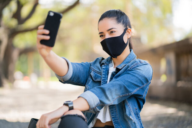 女人戴着面具的年轻女子在户外用手机自拍的照片时尚肖像面具