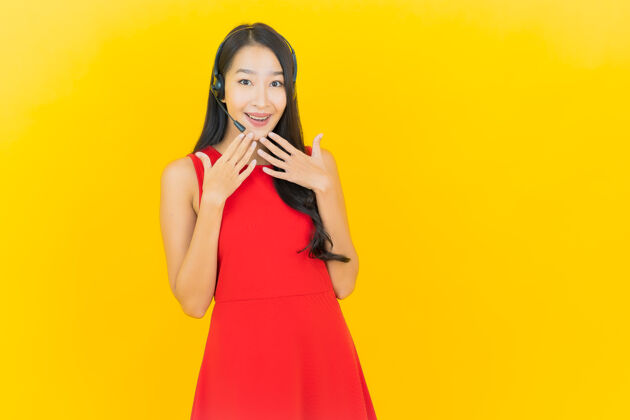 耳机肖像美丽的亚洲年轻女子与耳机沟通和支持呼叫中心服务黄墙耳机商务女性微笑