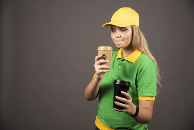 人年轻的女送货员拿着咖啡杯在黑暗的背景高品质的照片女女士帽子