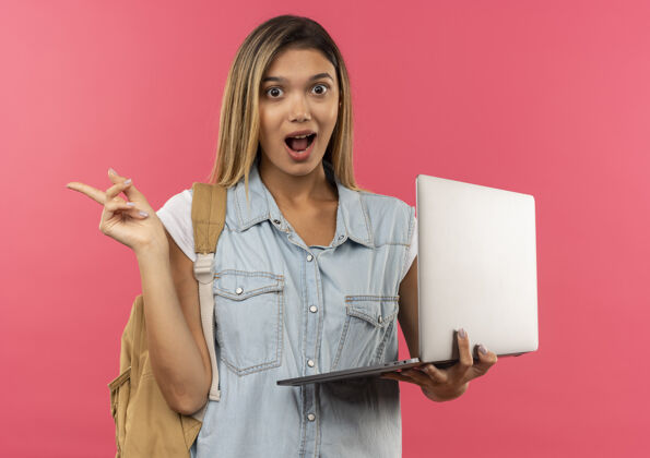 背部令人印象深刻的年轻漂亮的女学生穿着背包拿着笔记本电脑 指着粉红色的隔离边笔记本电脑包年轻