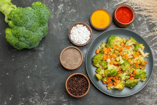 蔬菜上图：健康膳食 黑色盘子上放着花椰菜和胡萝卜 灰色桌子上放着香料花椰菜香料午餐