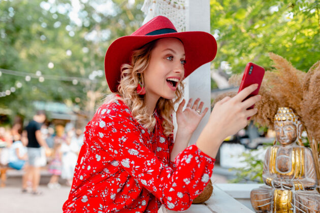 女士迷人的时尚金发微笑的女人在稻草红帽子和衬衫夏季时尚服装举行使用智能手机咖啡厅女性脸手机