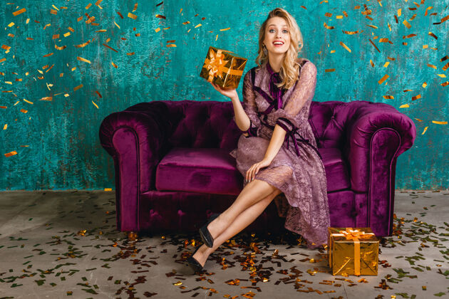 漂亮穿着时尚紫罗兰色晚礼服的迷人女人坐在天鹅绒沙发上 带着礼物花式庆典服饰