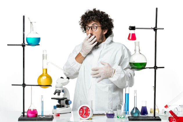化学正面图身穿白色特殊套装的年轻男性科学家站在桌子旁 拿着解决方案外套视图医学