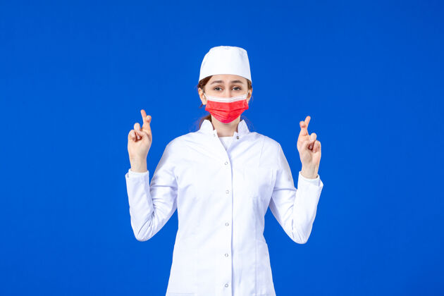 年轻护士正面图身着医疗服的年轻护士 蓝色墙上戴着红色防护面具前线人医院