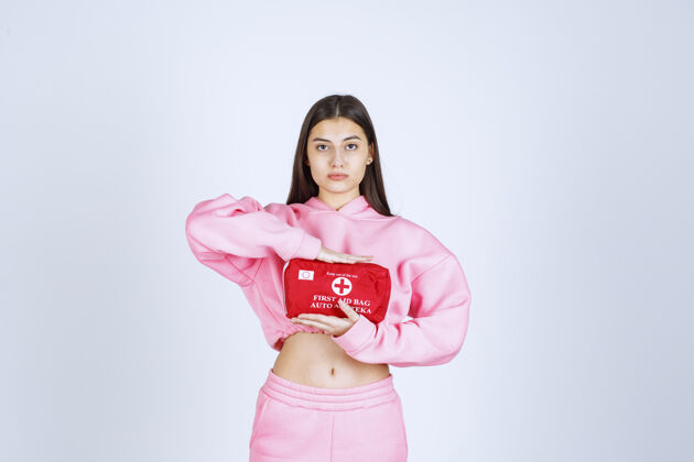 满意穿着粉色睡衣的女孩拿着一个红色的急救箱在宣传销售服装年轻