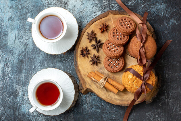 顶视图饼干和饼干茴香肉桂棒圆木板两杯茶在黑暗的桌子上深色热的茶碟