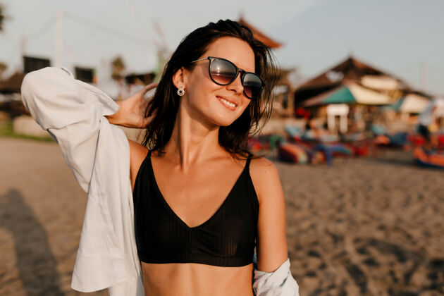 运动员迷人可爱的黑头发女孩穿着黑色上衣和衬衫在沙滩上阳光下的户外肖像放松美丽沙滩