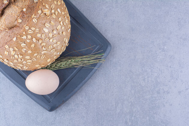 鸡蛋一个鸡蛋 一条面包和一根麦秆放在大理石表面的木板上面粉面包外套