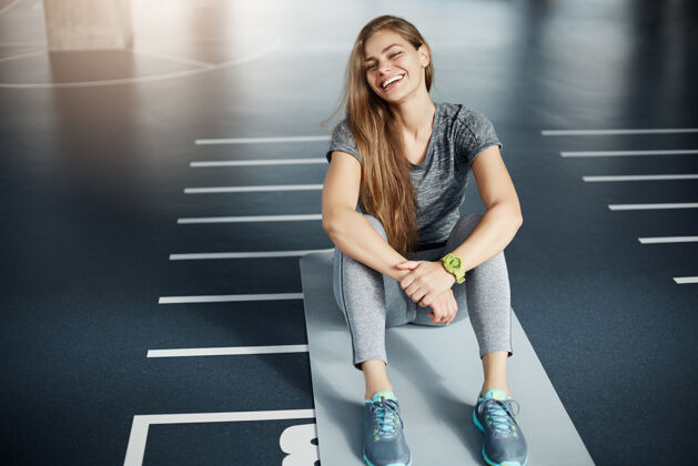 室内一位年轻的女健身教练坐在空荡荡的空间里 经过长时间的艰苦锻炼 她笑了健身理念强壮肌肉准备