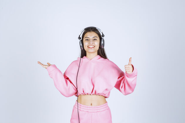 照片穿着粉色睡衣的女孩戴着耳机 展示着享受的标志高质量的照片交易姿势人类