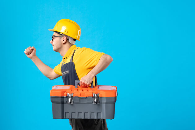 箱子前视图运行男建设者制服与工具箱在他的手上的蓝色服务修理工头盔