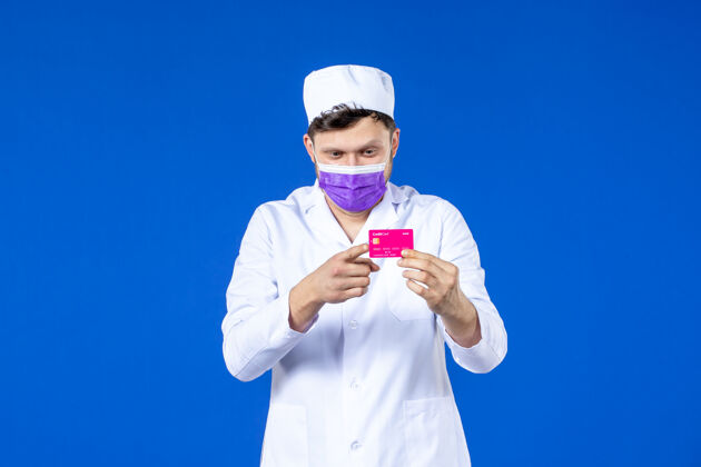 诉讼前视图中的男医生穿着医疗服和面具持有信用卡的蓝色男医生医学病毒