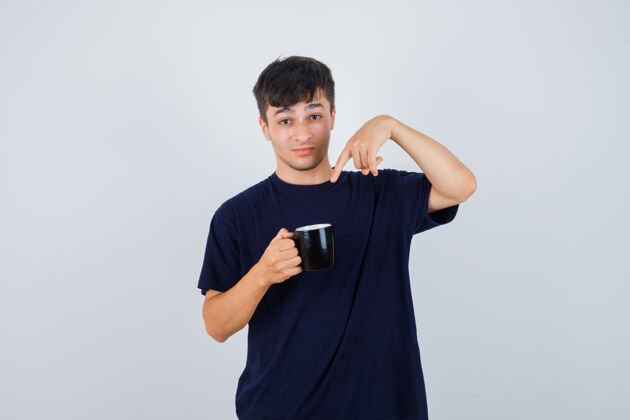 茶年轻人指着一杯茶 穿着黑色t恤衫 神情困惑前视图问题时尚指向