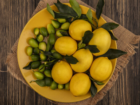 新鲜新鲜水果的俯视图 例如柠檬和金盏花 放在木制表面的麻袋布上的黄色盘子上配料素食柠檬