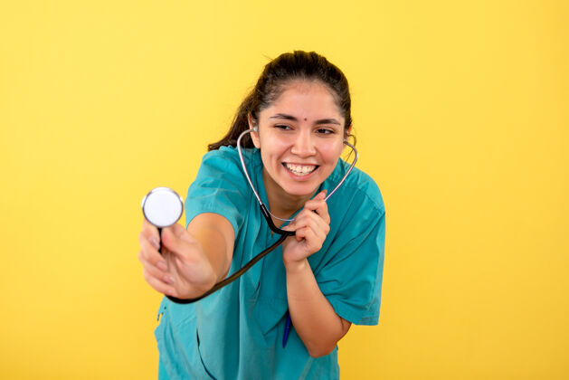 高尔夫球手正面图快乐的年轻女医生 带听诊器站在黄色背景上医院站成人