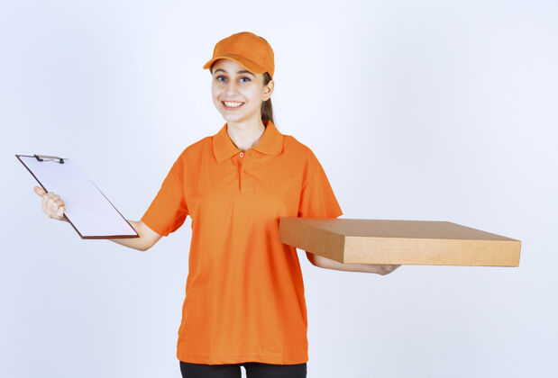 成人身着橙色制服的女快递员手里拿着一个外卖比萨饼盒和一个通讯录智能姿势安全