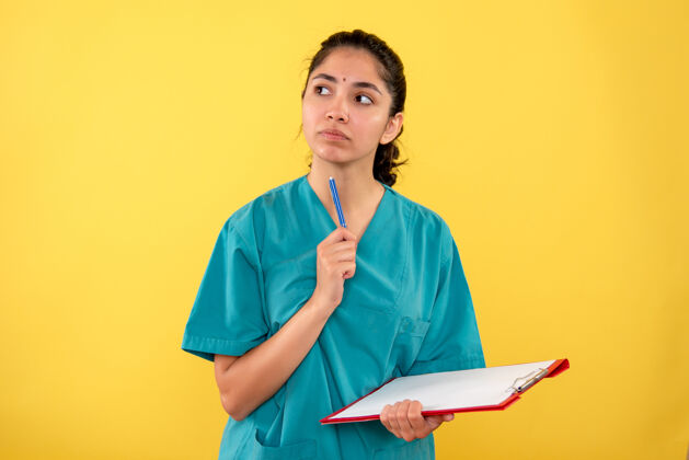 持有前视图穿着制服的体贴的女医生拿着剪贴板和黄色背景上的笔女医生工作思想