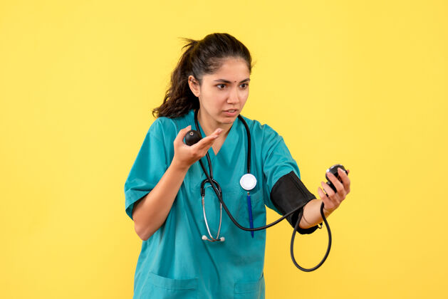 听诊器正面图美丽的女医生穿着制服站在黄色背景上检查血压计制服健康护士