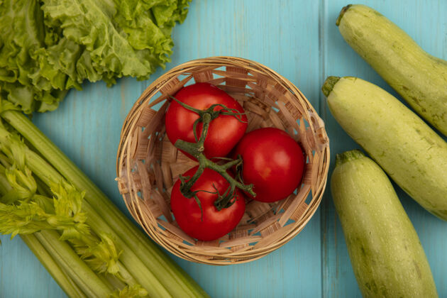 美味顶视图美味的西红柿桶与莴苣西葫芦和芹菜隔离在一个蓝色的木制表面新鲜配料养殖