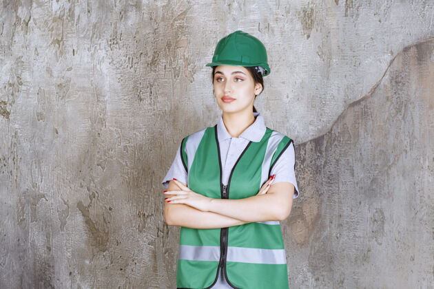 经验丰富女工程师身穿绿色制服 戴着头盔交叉双臂 看上去很专业维修成人聪明