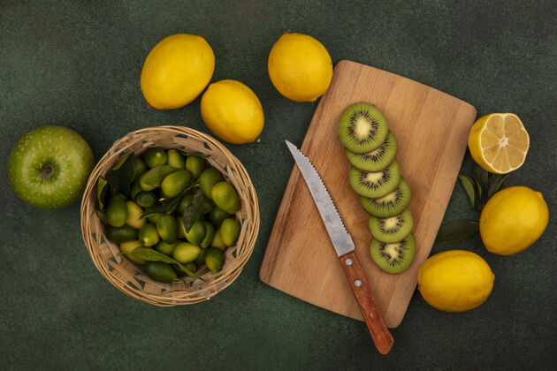 新鲜木制菜板上美味的猕猴桃切片俯视图 桶上放着小刀和金盏花 柠檬和苹果被隔离在绿色的表面上苹果成熟木材